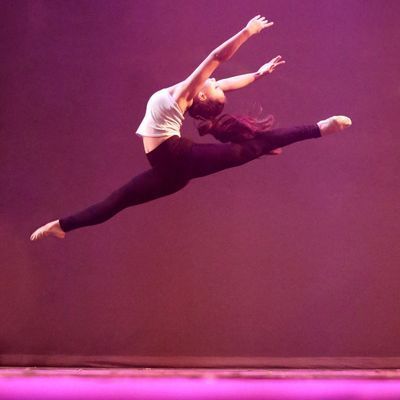 A woman in a white top and black pants is jumping in the air