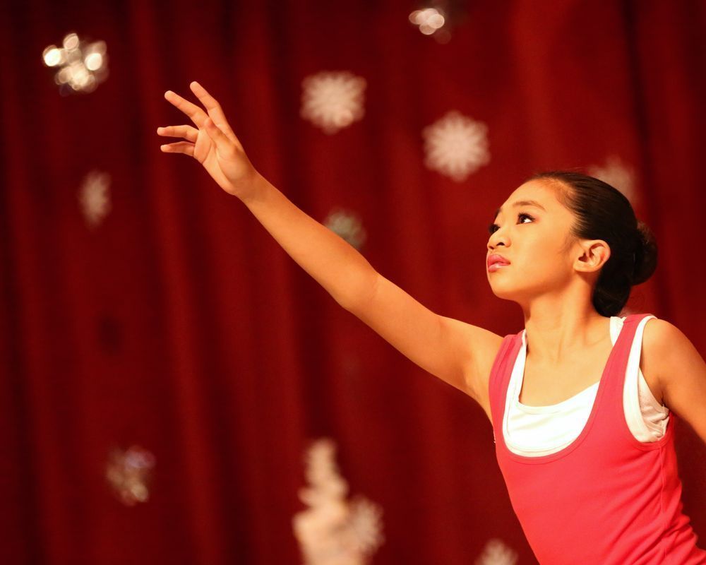 A young girl in a pink tank top is reaching for something