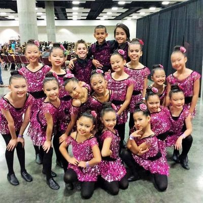 A group of young girls in pink sequined dresses pose for a picture