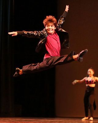 A man in a red shirt is jumping in the air on a stage.