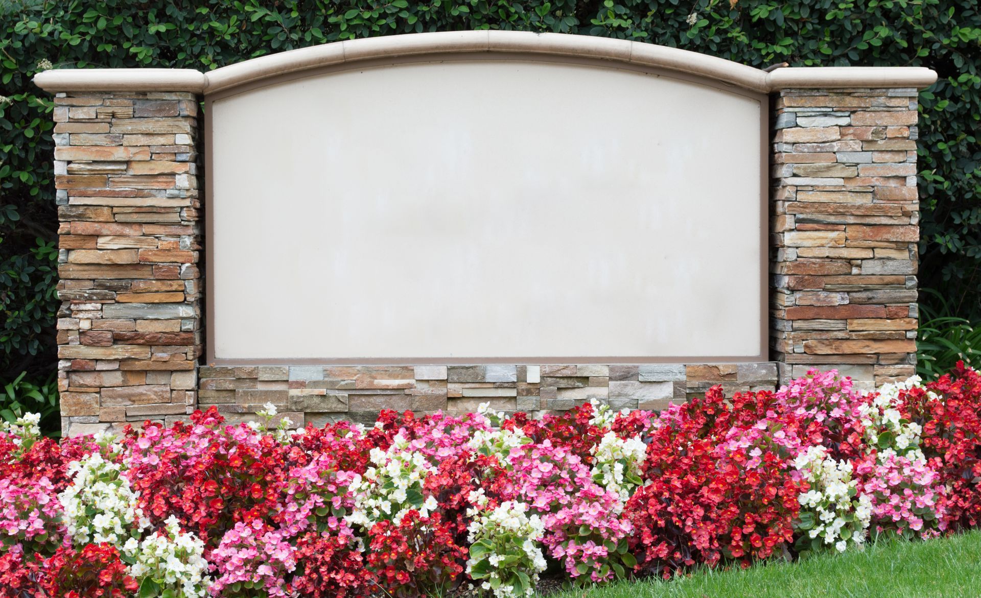 Single monument maker stone memorial sign with stacked stone pillars and landscaped flower bed.