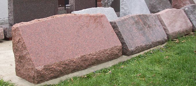 A row of reddish-brown granite headstones sit on a grassy area.
