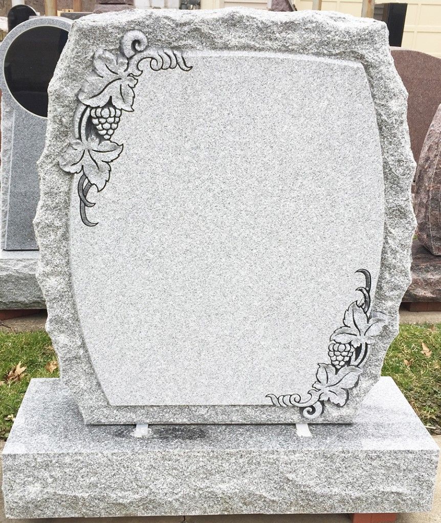 Gray granite tombstone with carved grapevines, set on a stone base.