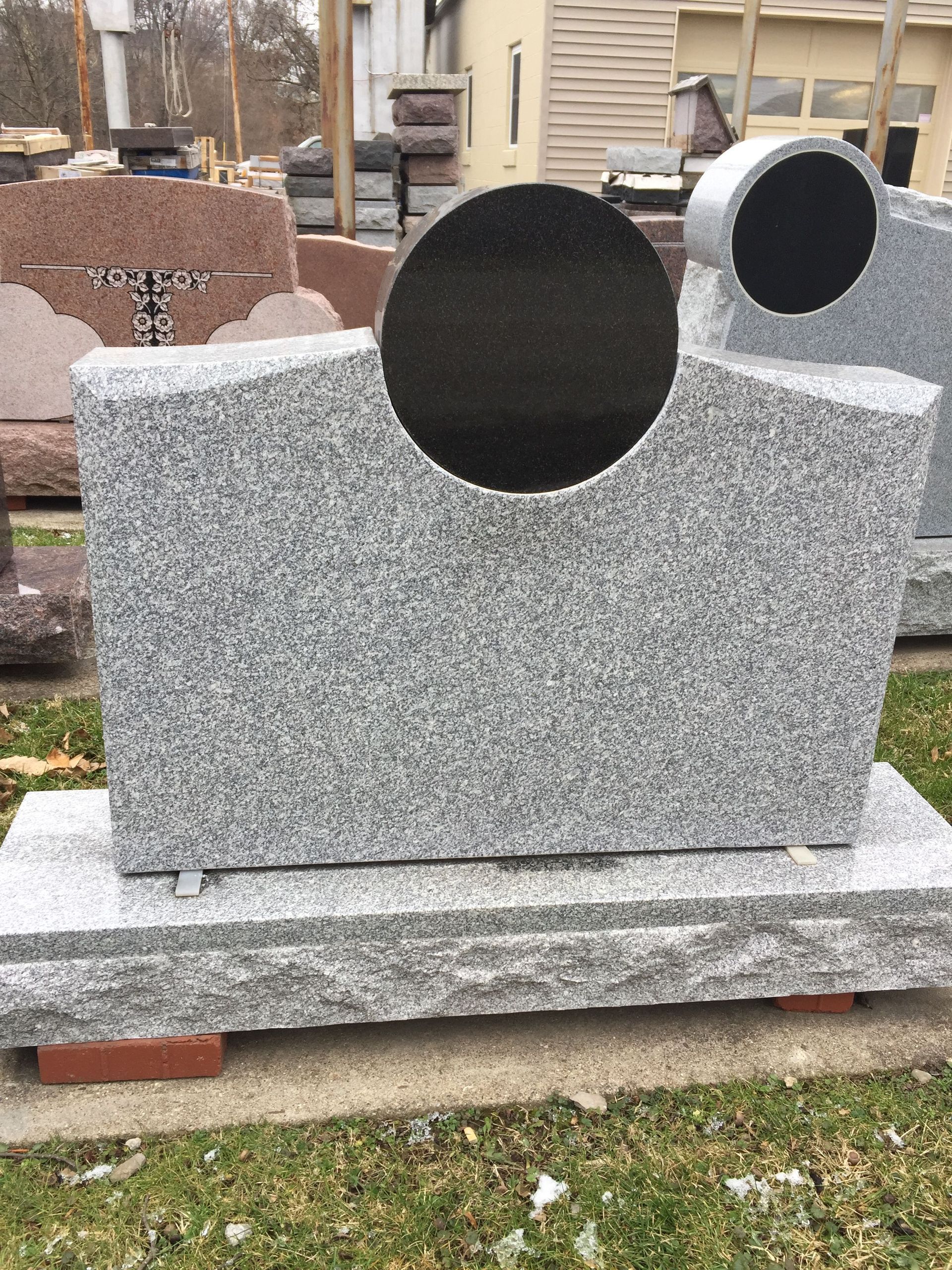 Gray granite headstone with a circular cut-out, set on a base in an outdoor display.