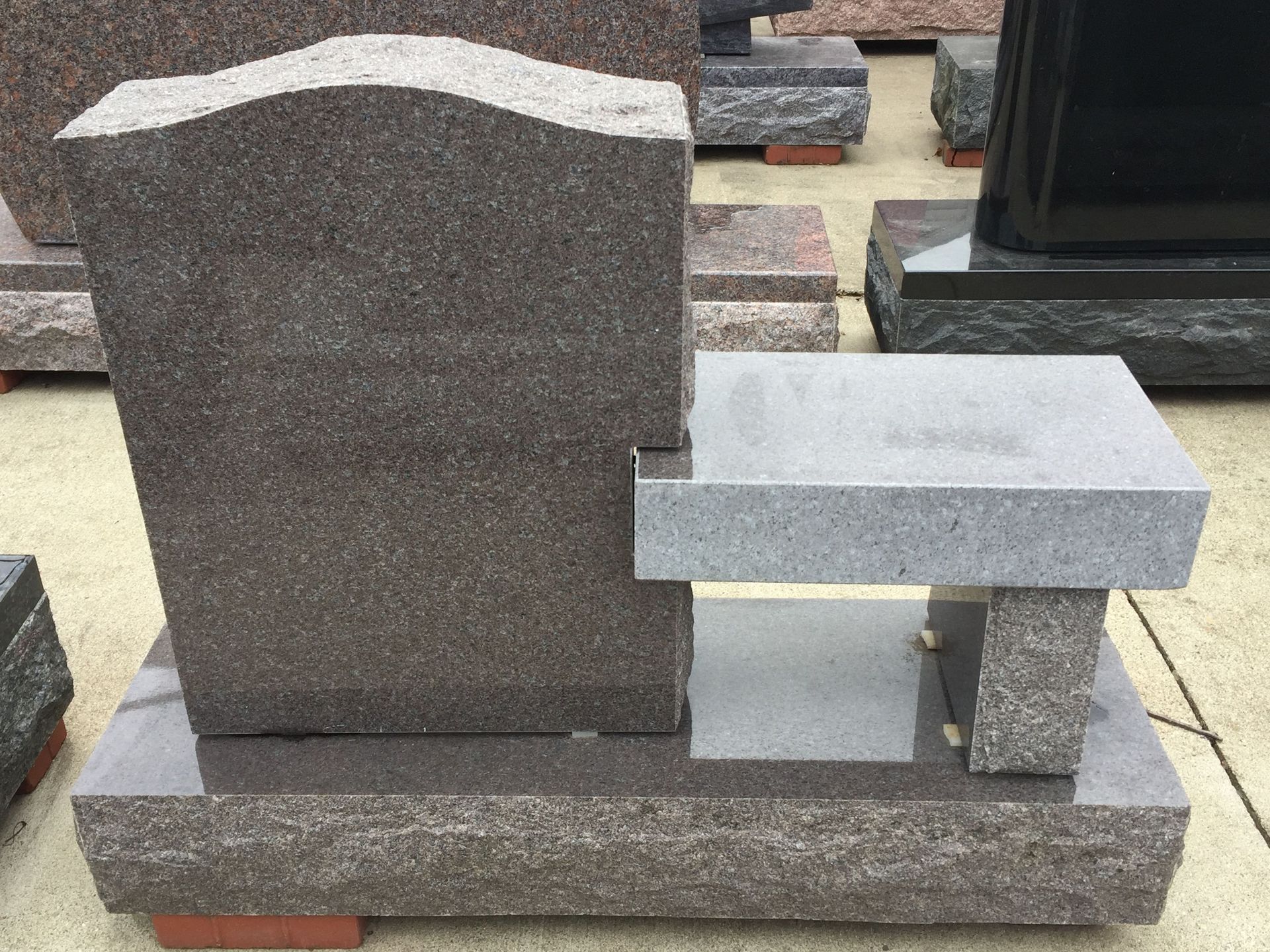 Gray granite headstone with attached bench, resting on a polished base, outdoor setting.