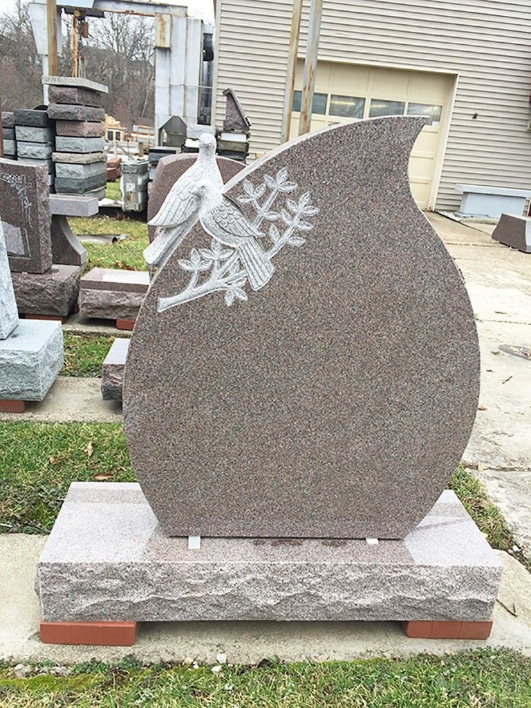Gravestone shaped like a teardrop with doves and foliage carving. Brown stone on a pink granite base.