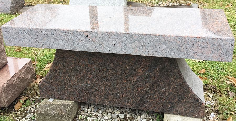 Granite bench in shades of brown and pink, on a stone base outdoors.