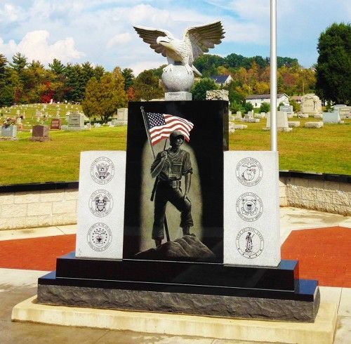 Monument with an American flag-holding soldier, an eagle statue, and service branch emblems in a cemetery.