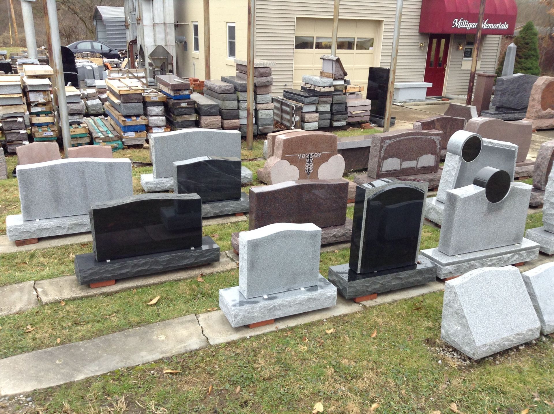 Headstones on display in a yard, with a building in the background.