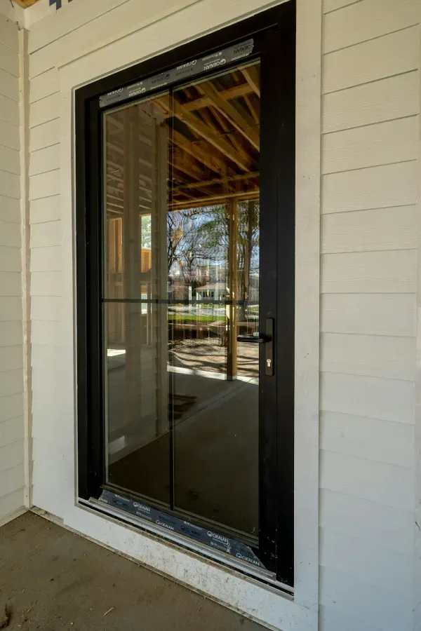 A sliding glass door is being installed on the side of a house under construction.
