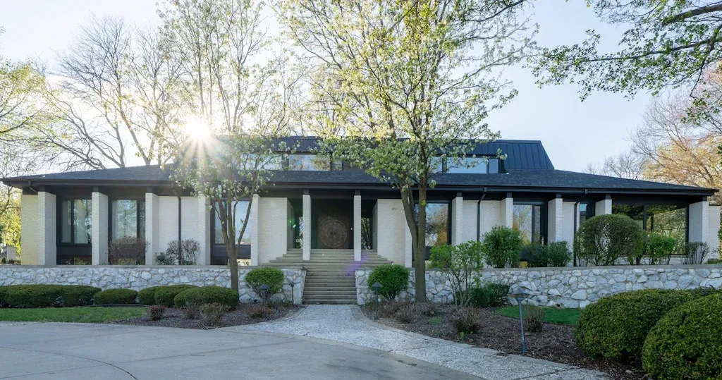 The sun is shining through the trees in front of a large house.