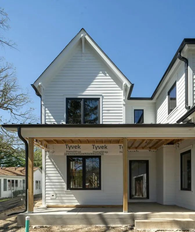 A white house with black windows and a porch is under construction.