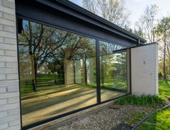 A house with a lot of windows and trees reflected in the windows.