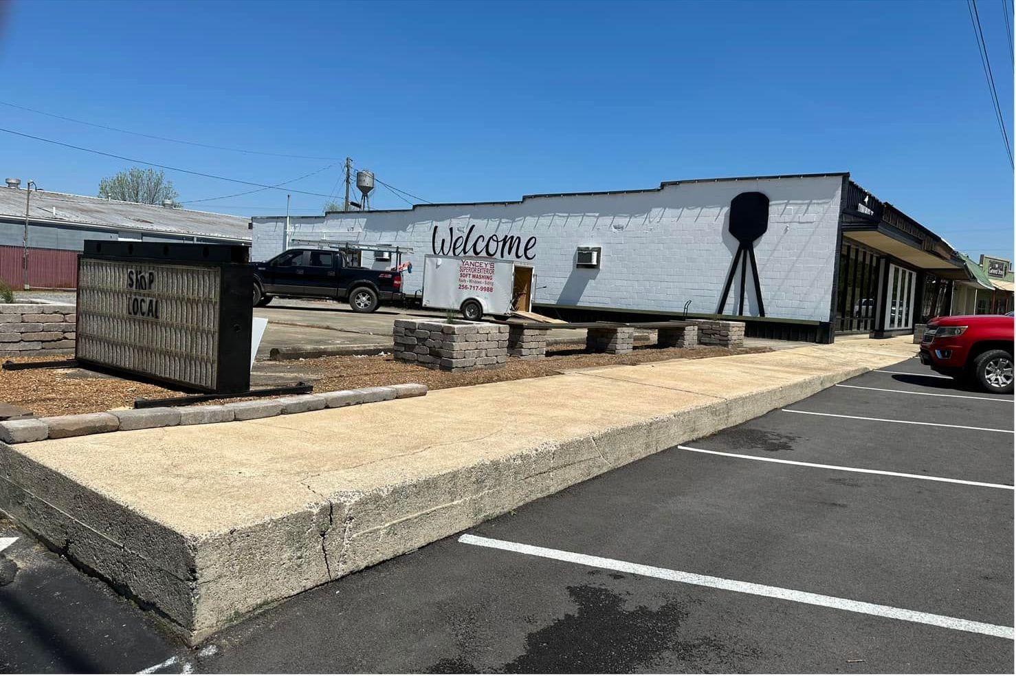 A white building with the word welcome on it is sitting in a parking lot.
