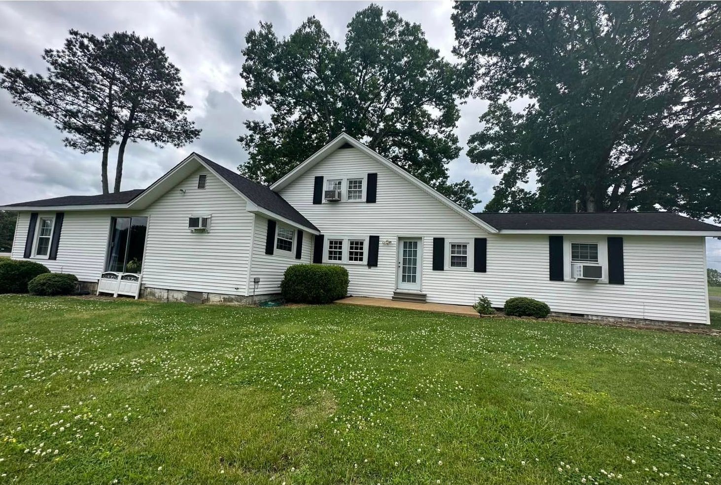 A white house with black shutters is sitting on top of a lush green field.