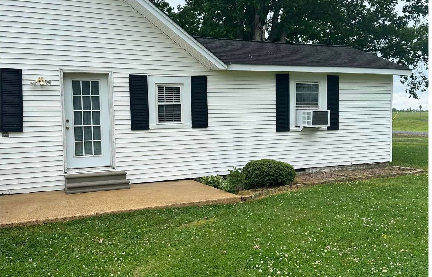 A white house with black shutters is sitting on top of a lush green field.