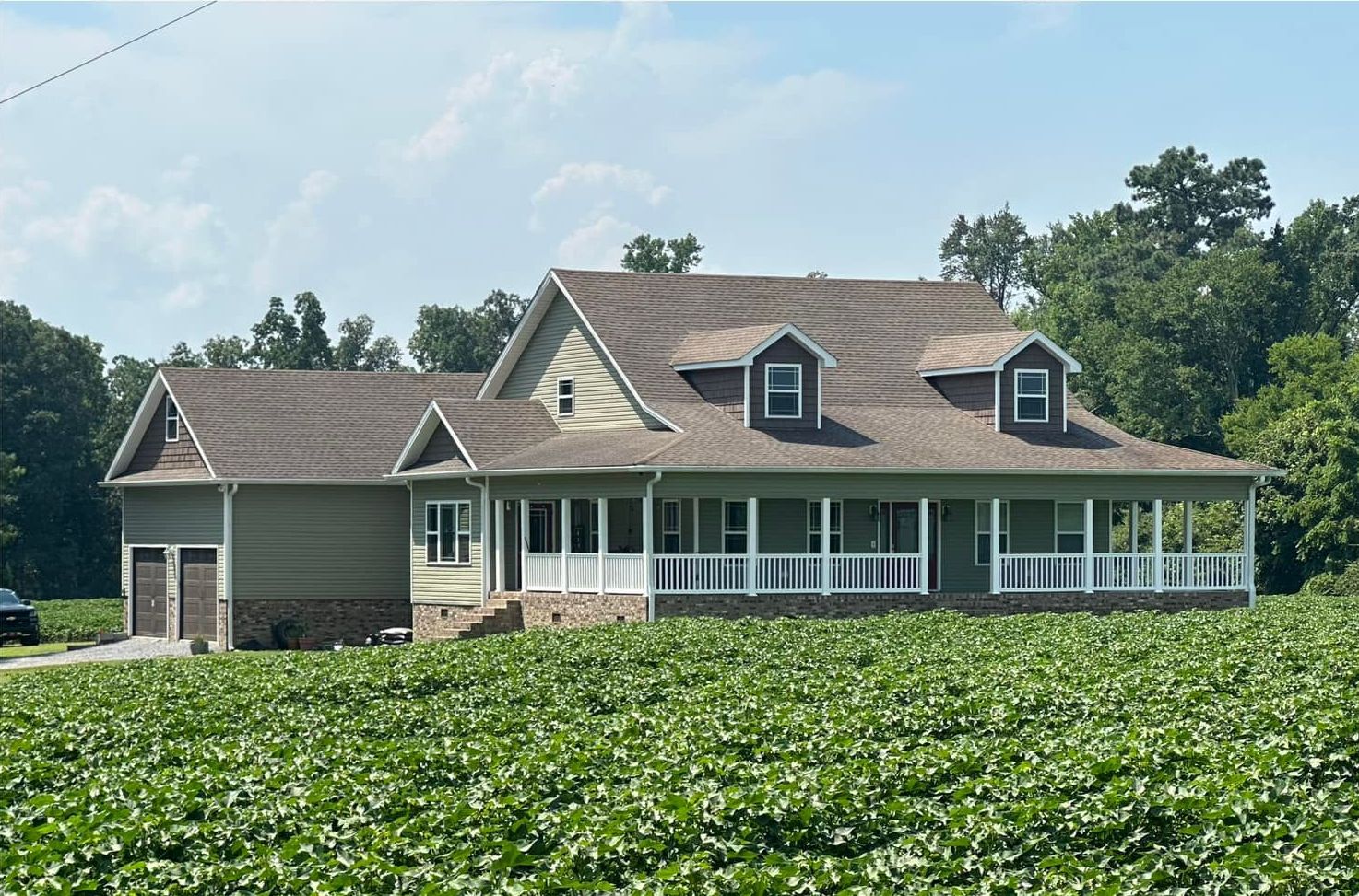A house with a porch is sitting in the middle of a field.