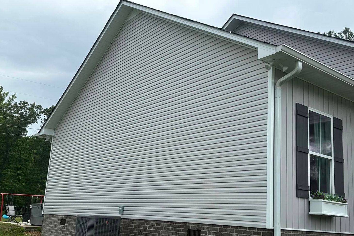 The side of a house with a white siding and black shutters.