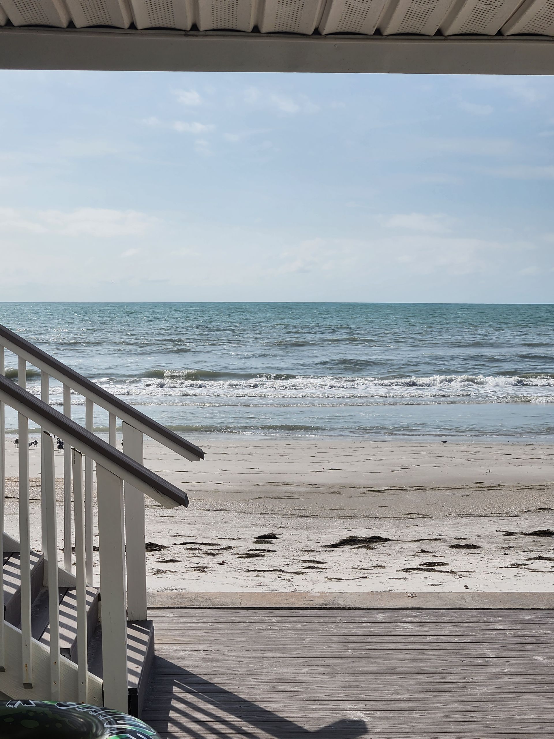 View from porch steps to beach, ocean under blue sky.
