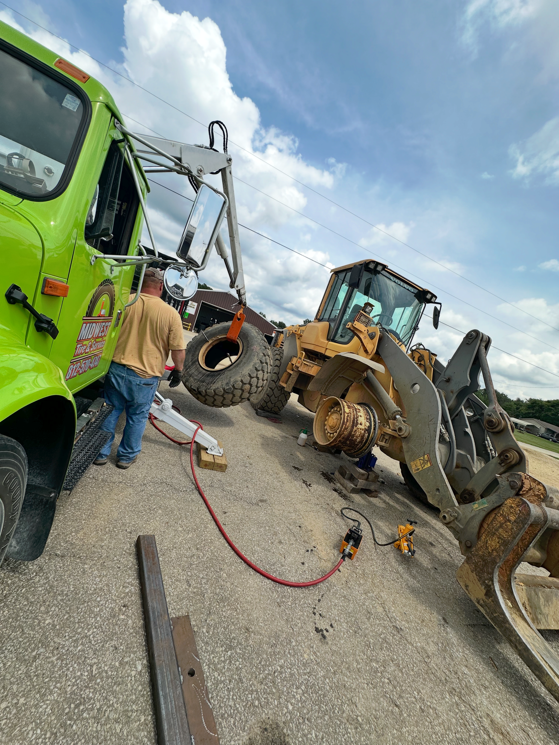 Tow truck attempting to right a yellow construction loader on a road, man nearby. | Midwest Tire & Service LLC