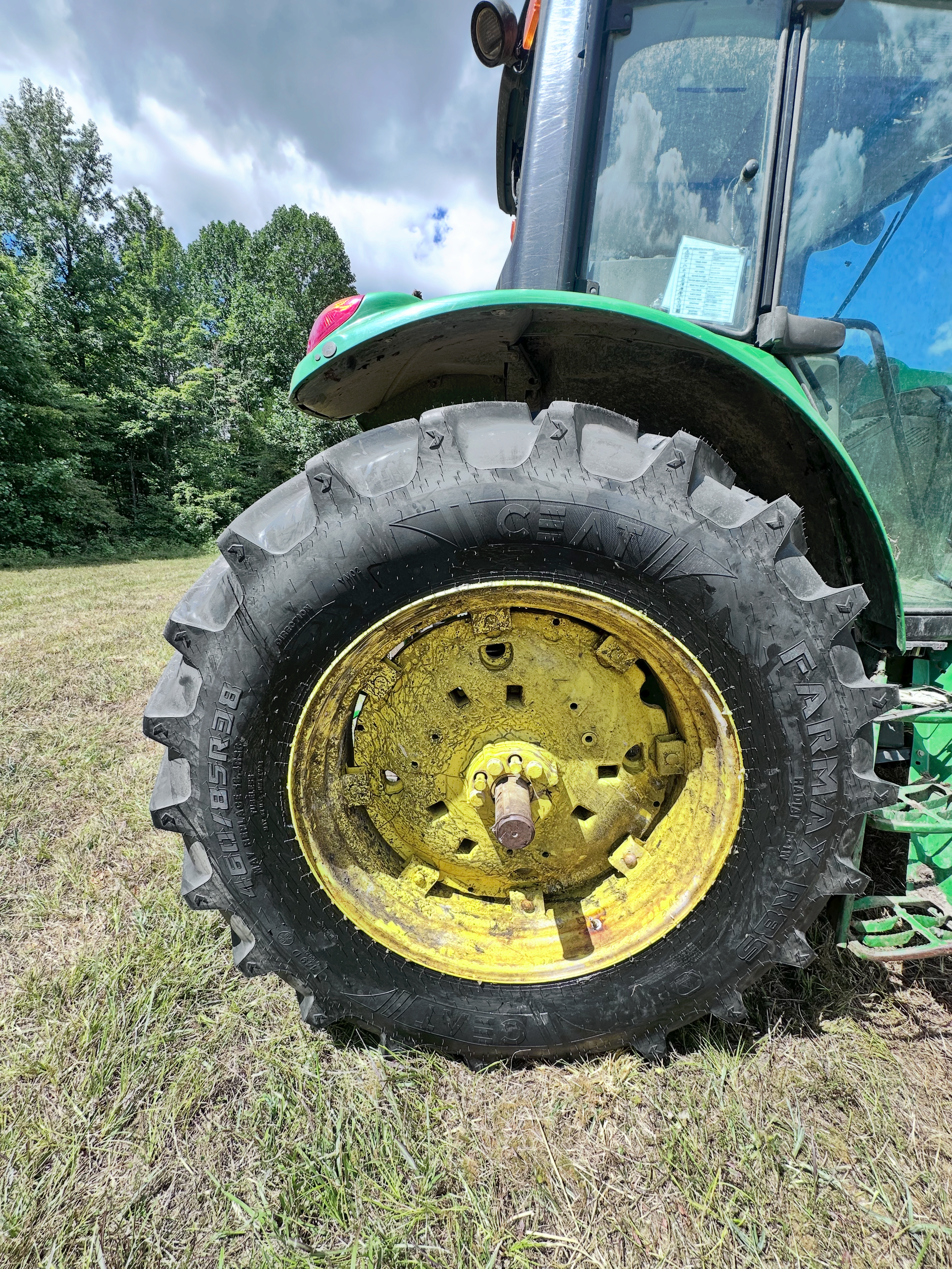 Side view of a green John Deere tractor wheel on a grassy field; yellow wheel, black tire. | Midwest Tire & Service LLC