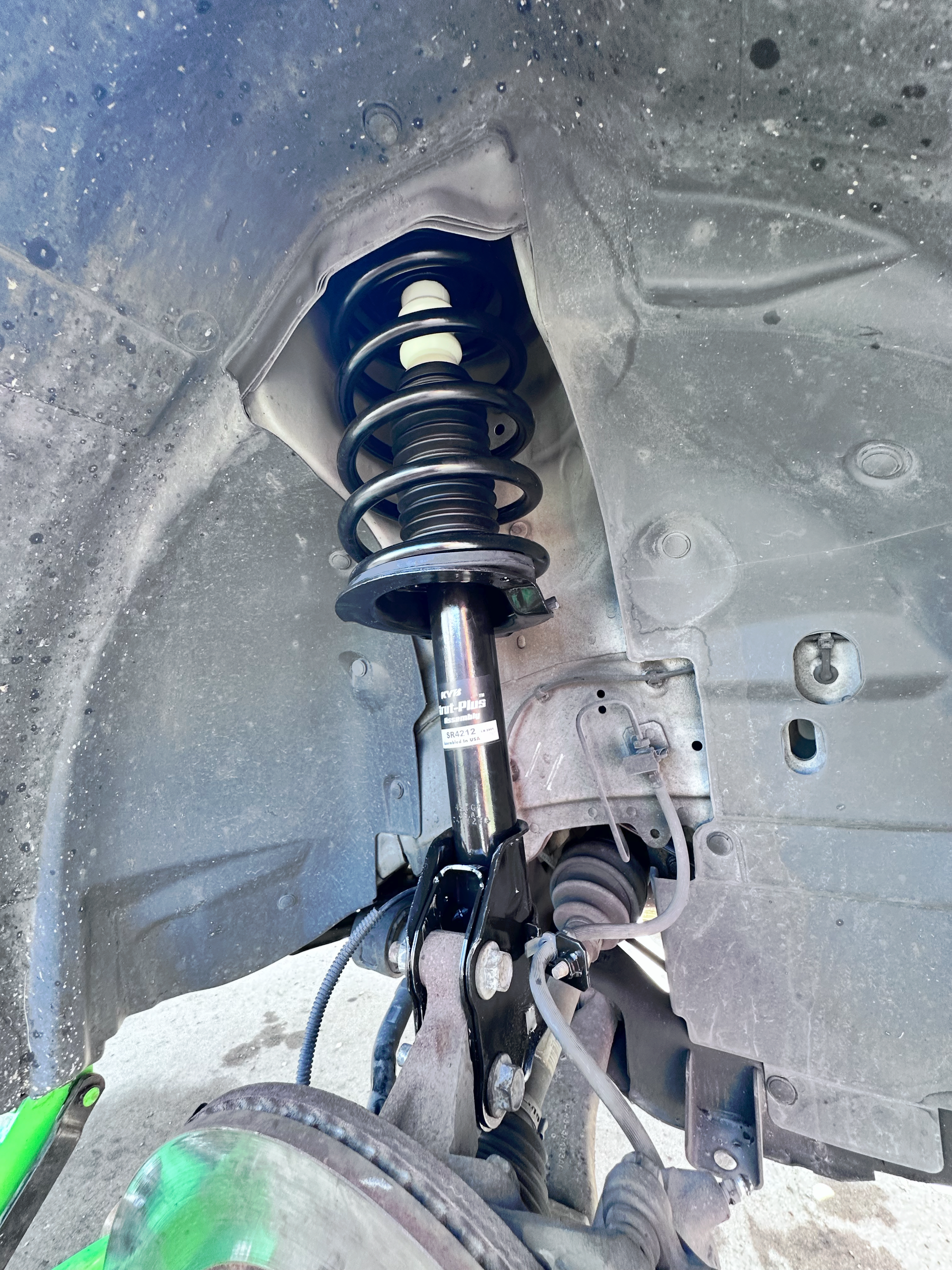 Car's front wheel suspension system, visible shock absorber and coil spring within the wheel well. | Midwest Tire & Service LLC