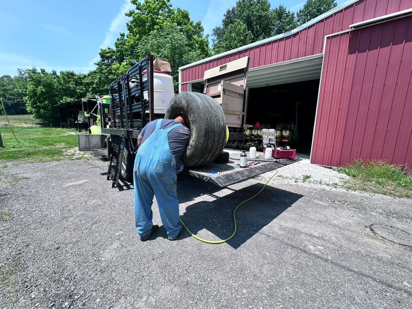Person in Blue Overalls Changing a Large Tire on a Truck Outside a Red Building | Midwest Tire & Service LLC