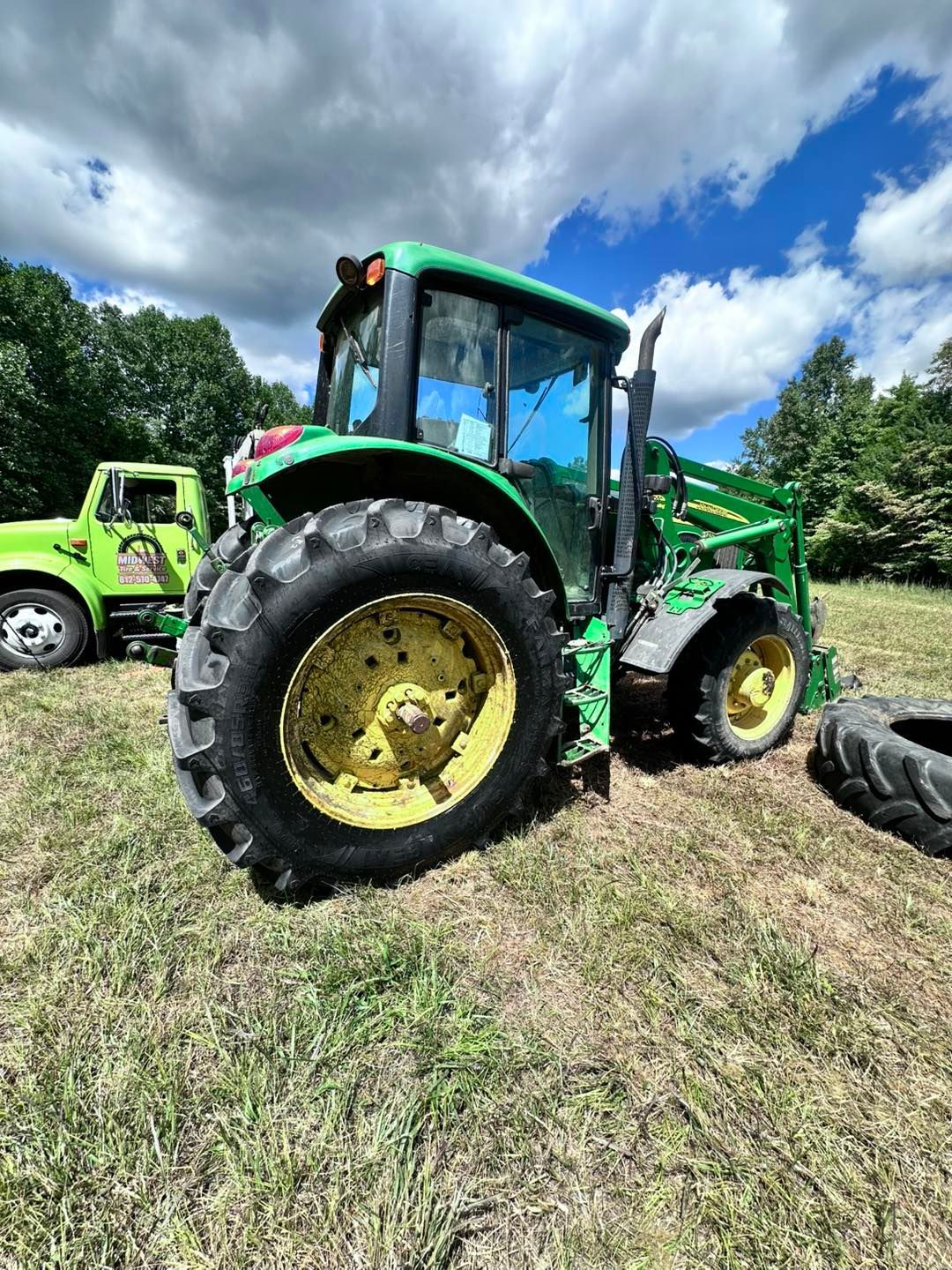 Green John Deere Tractor Parked in a Field on a Sunny Day with a Cloudy Sky | Midwest Tire & Service LLC