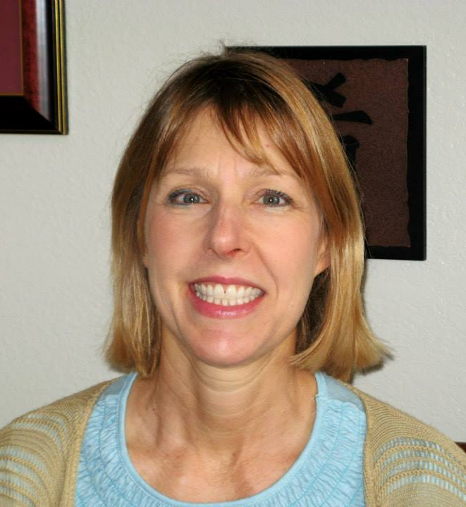A woman wearing a blue shirt and a tan cardigan smiles for the camera