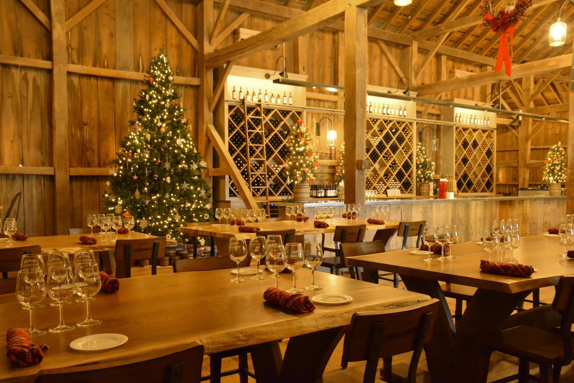 Inside a rustic barn restaurant, decorated for Christmas; tables set, tree in background.