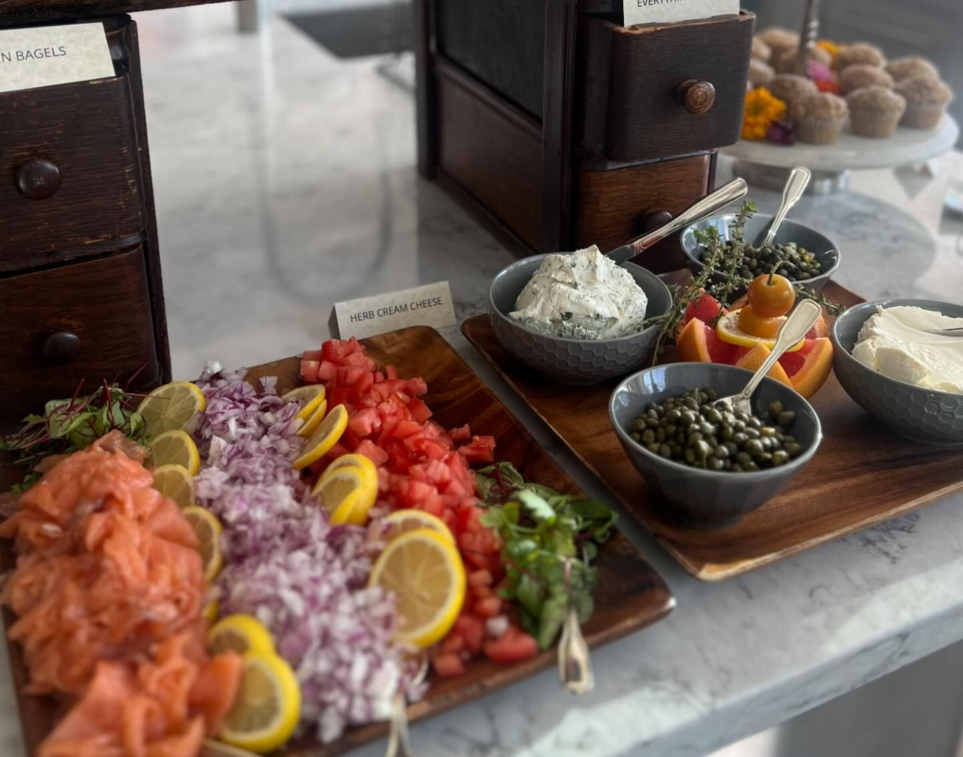 Smoked salmon and bagel bar with toppings: tomatoes, onions, capers, cream cheese, and muffins.