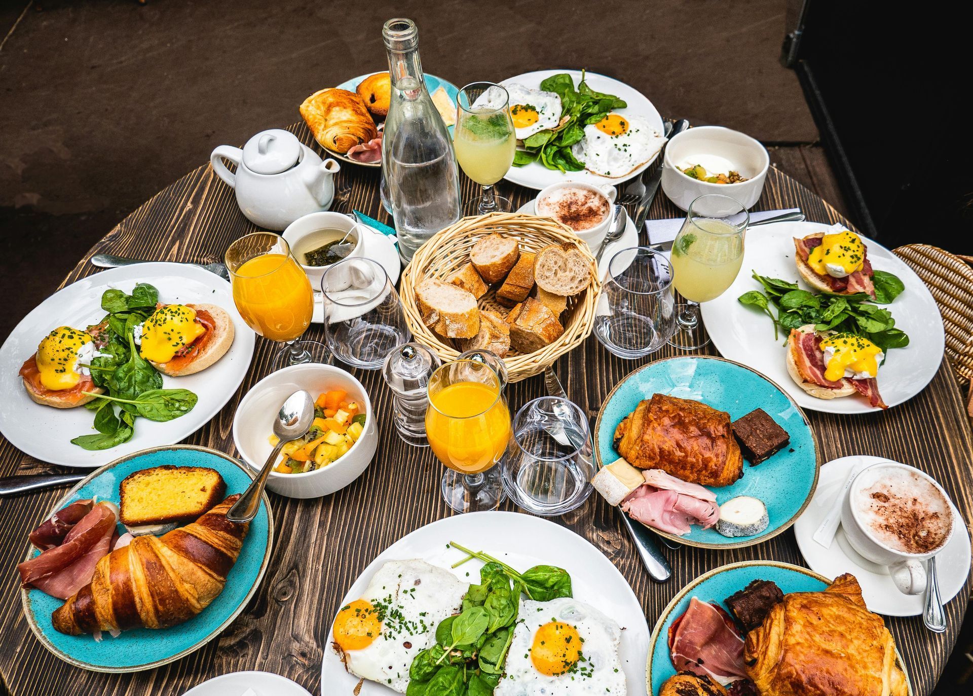 Shared dining table with assorted dishes, bread, fruit, drinks, and a wine bottle overhead view