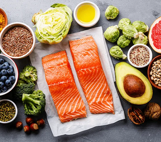 Salmon fillets with various healthy foods like vegetables, fruit, nuts, and seeds.