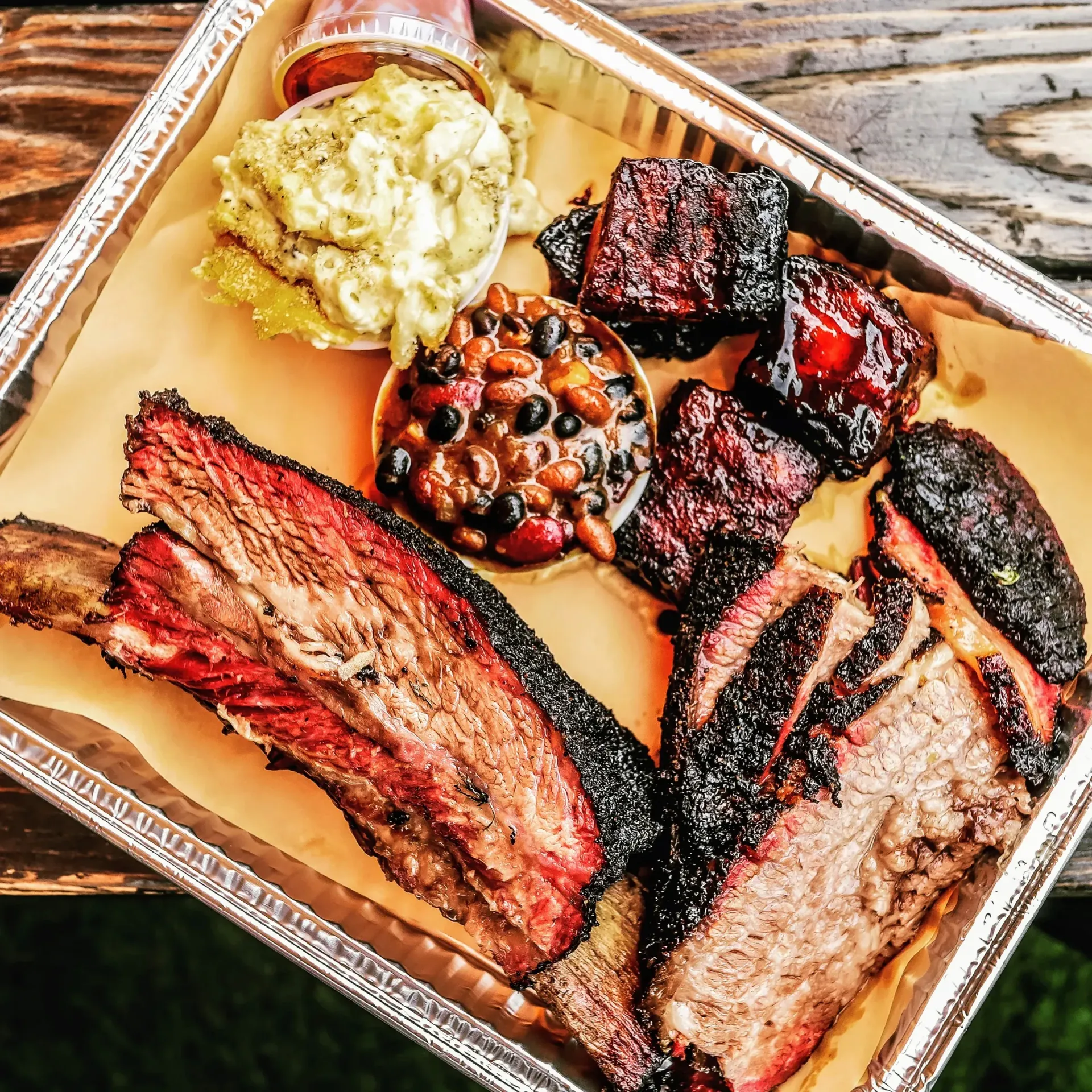 Barbecue catering with brisket, ribs, beans, mac & cheese, and sauce in a metal tray.