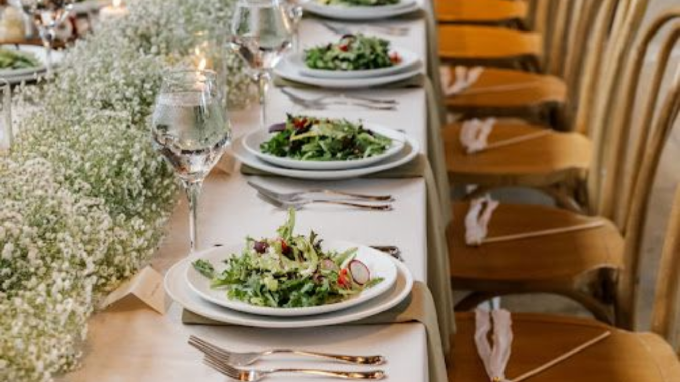 Elegant table setting with salad on white plates, floral centerpieces, and chairs.