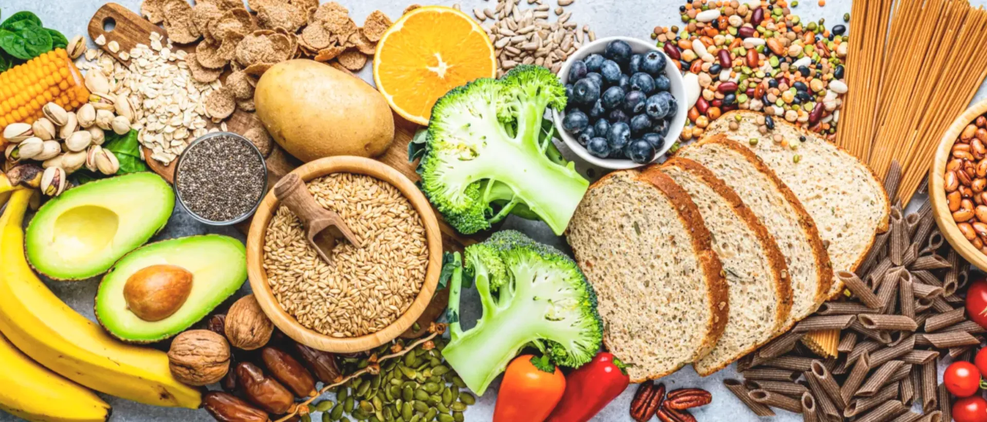 Assortment of fiber-rich foods like whole grain bread, broccoli, blueberries, avocado, nuts, and grains.