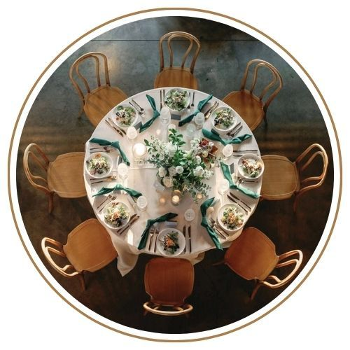 Overhead view of a round table set for a meal with eight chairs. White tablecloth, floral centerpiece.