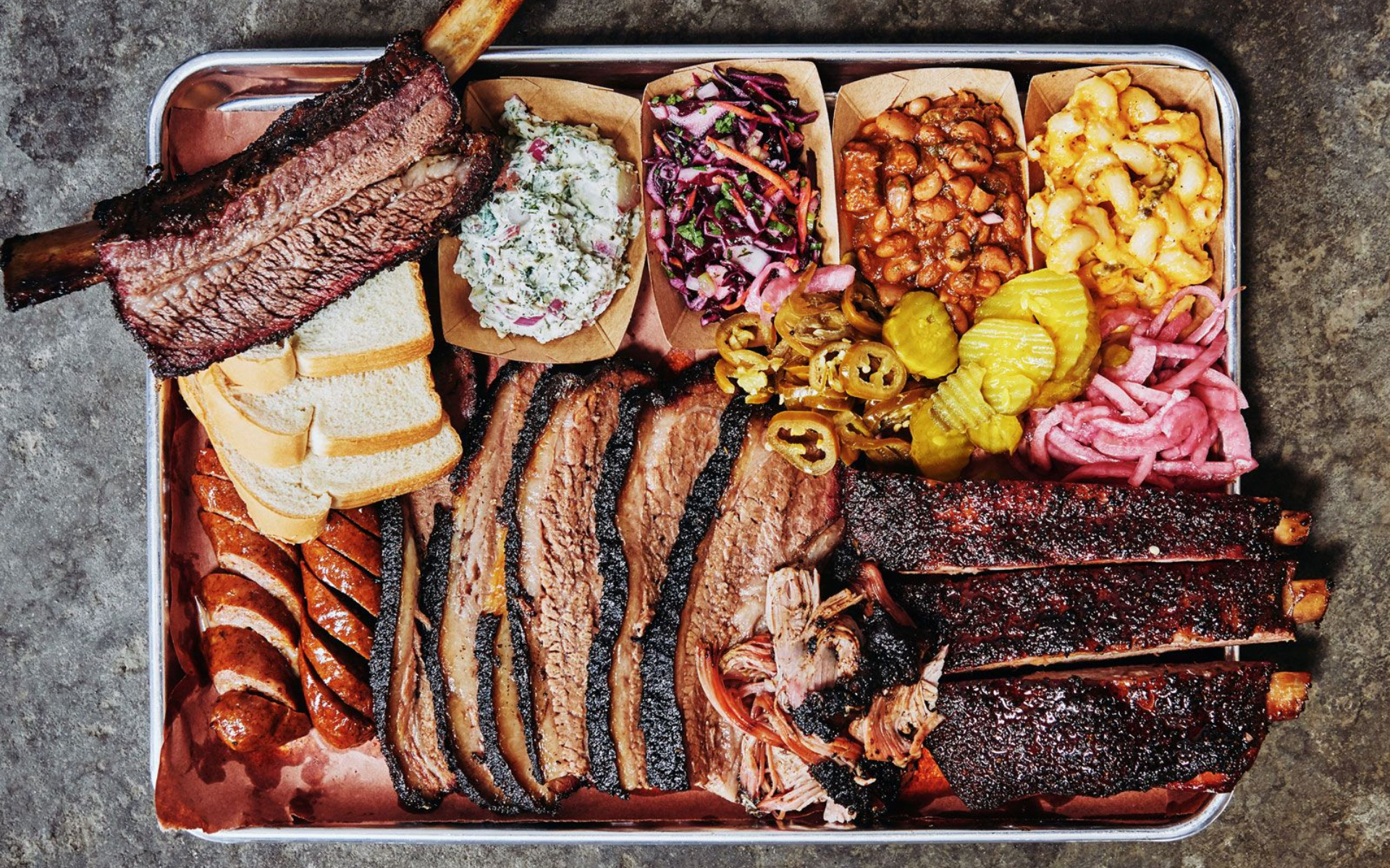 Barbecue platter: smoked brisket, ribs, sausage, sides (coleslaw, beans, mac & cheese, pickles).