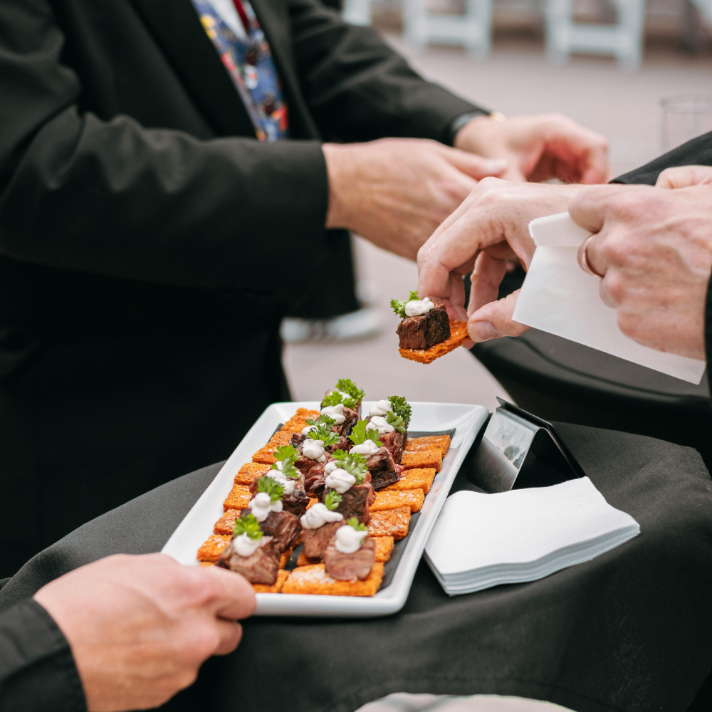 Hands serving bite-sized appetizers from a tray at a formal event