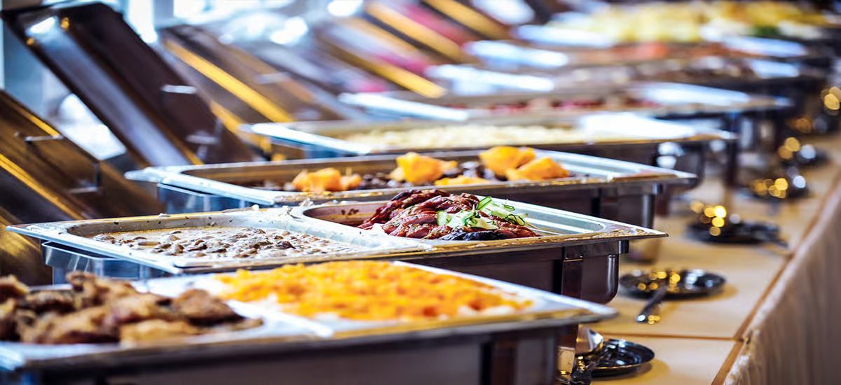 A long buffet table featuring multiple metal chafing dishes filled with various hot food options.