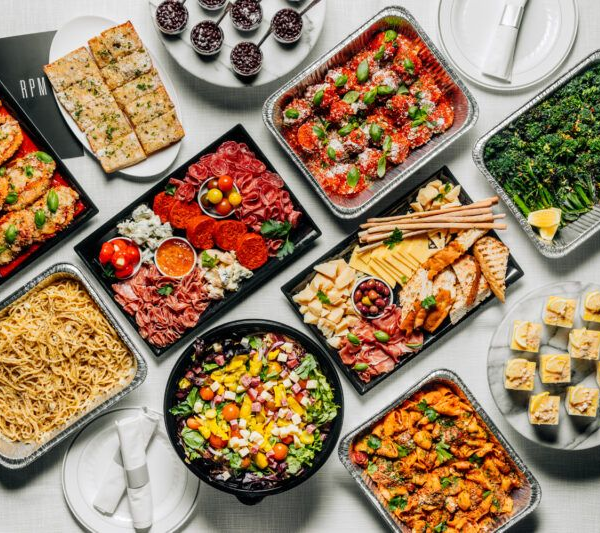 Assortment of catered dishes: pasta, salad, appetizers, charcuterie, and desserts, on a white surface.