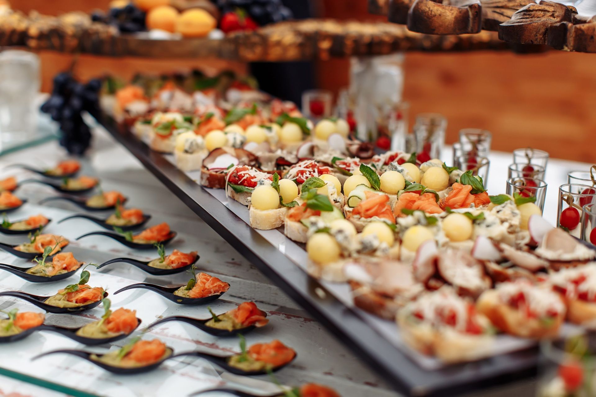 Buffet table with various appetizers, including small bites, in different colors, arranged on trays and spoons.