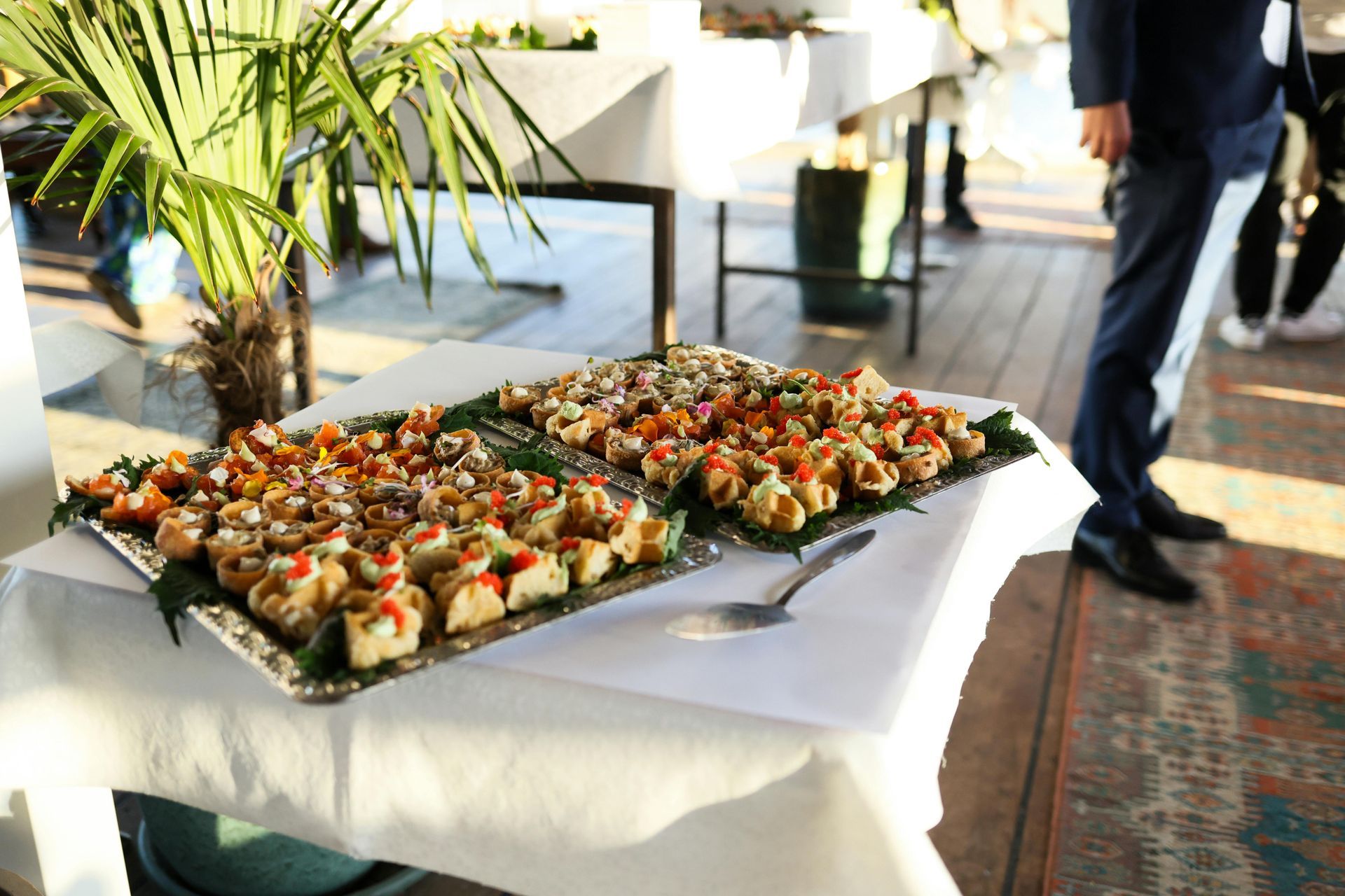Buffet table with appetizer platters at a bright indoor event, with people walking by
