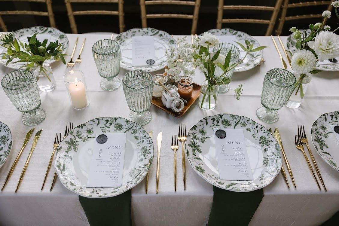 Elegant table setting with green and gold accents, plates, glasses, flowers, and menu cards