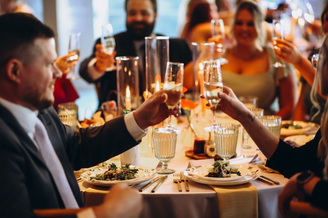 Guests at a formal dinner gathering clinking glasses in a celebratory toast, with blurred people in the background.