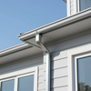 Close-up of a house roofline with white gutter and downspout against a blue sky