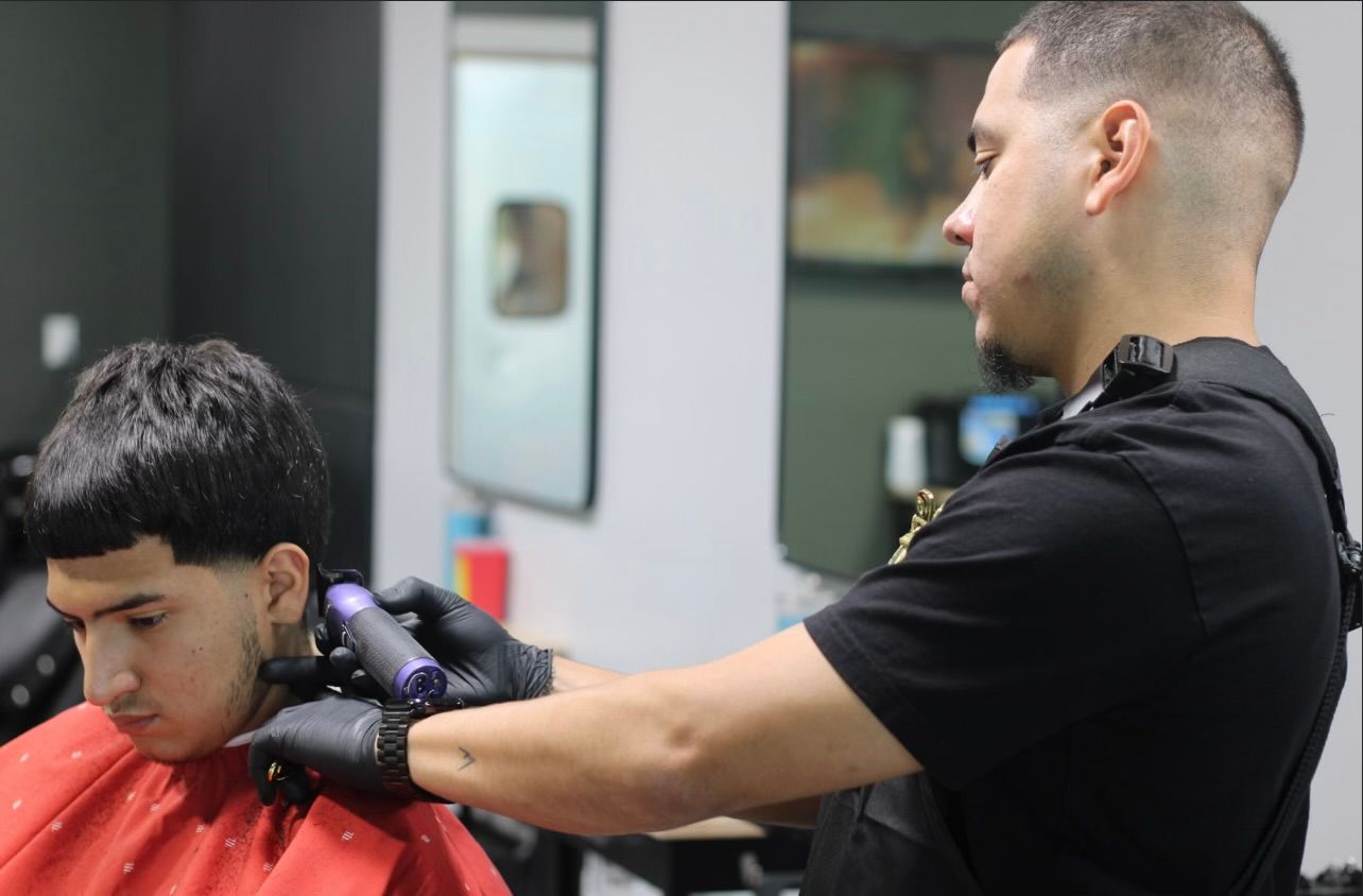 Barber giving a haircut with clippers in a salon. The customer has a red cape.