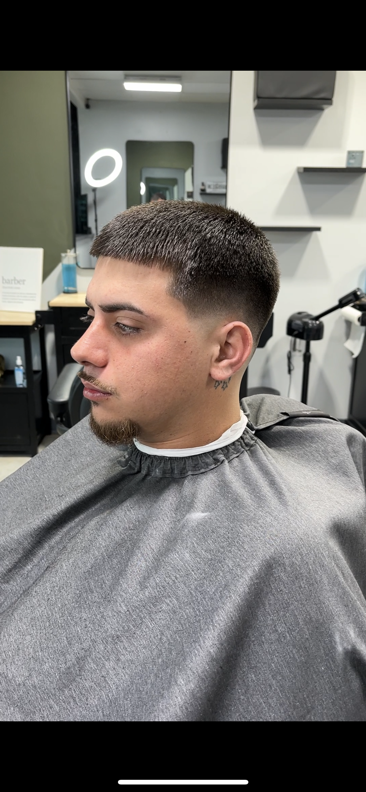 A man with a fresh haircut at a barbershop. He's wearing a barber's cape, profile view.