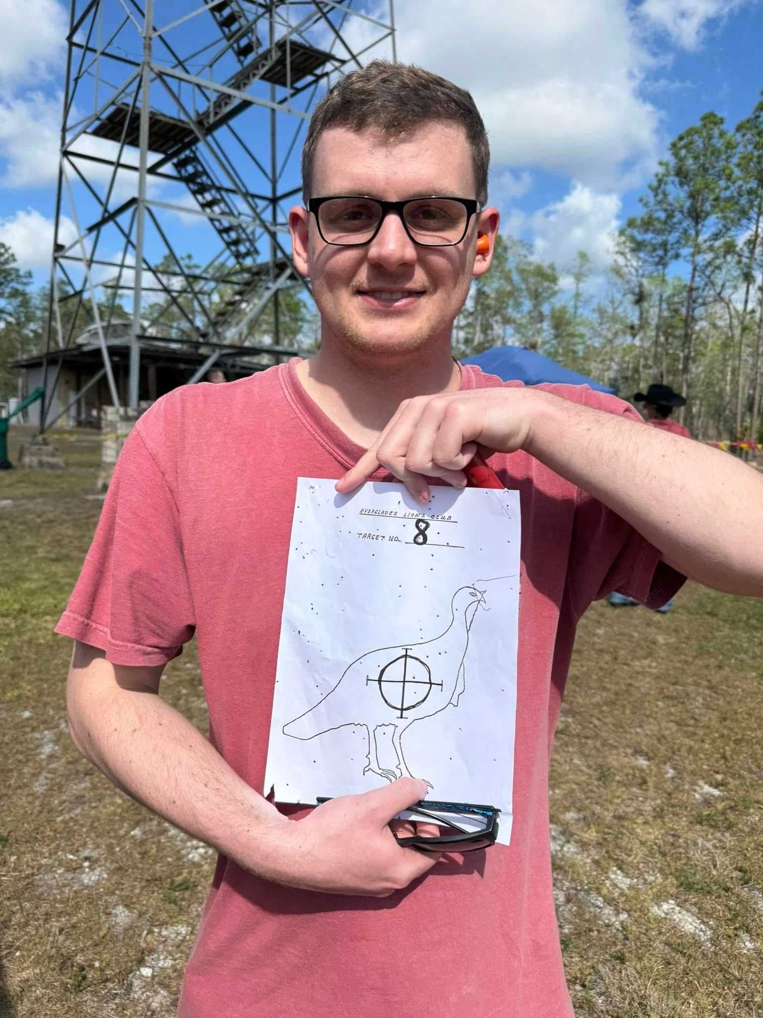 A man in a red shirt is holding a piece of paper with a drawing on it.