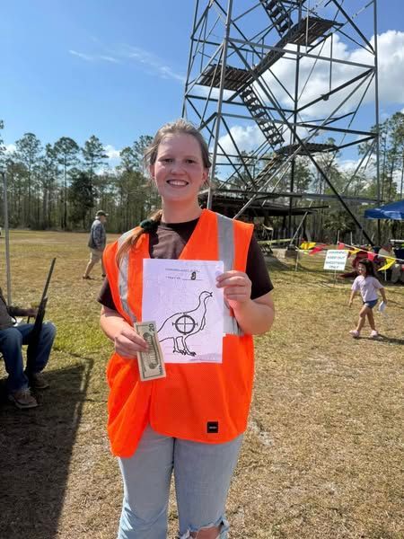 A woman in an orange vest is holding a drawing of an ostrich